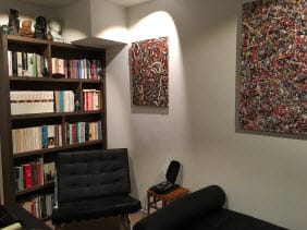 Praktijkruimte met boekenkast, leren zetels en abstracte schilderijen