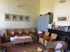 Groepsruimte met rieten stoelen, portretten en schouw
